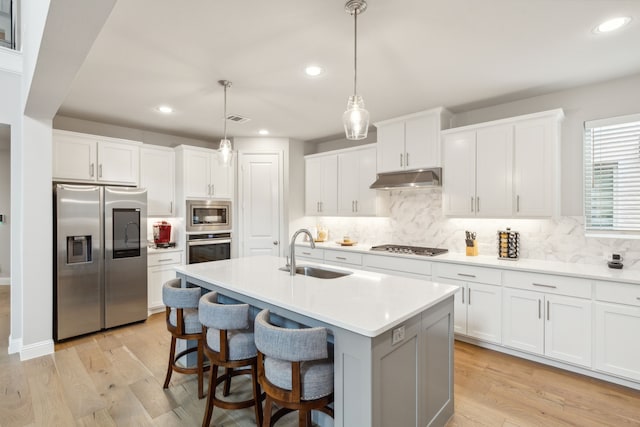 kitchen featuring a sink, light countertops, under cabinet range hood, appliances with stainless steel finishes, and light wood-type flooring