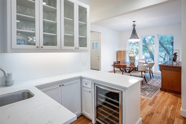 kitchen with pendant lighting, sink, white cabinetry, wine cooler, and light stone countertops