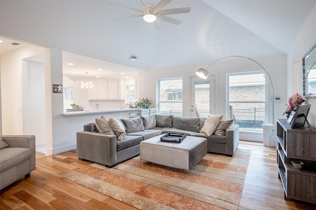 living room featuring high vaulted ceiling, ceiling fan with notable chandelier, and light wood-type flooring