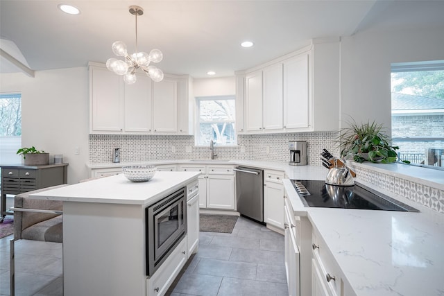 kitchen featuring decorative light fixtures, white cabinets, backsplash, light stone counters, and stainless steel appliances