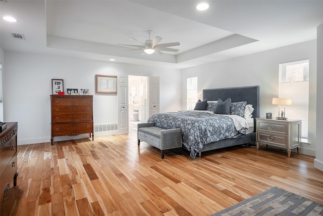 bedroom featuring a tray ceiling, light hardwood / wood-style floors, and multiple windows