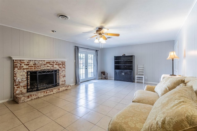 tiled living room with ornamental molding, a brick fireplace, ceiling fan, and french doors