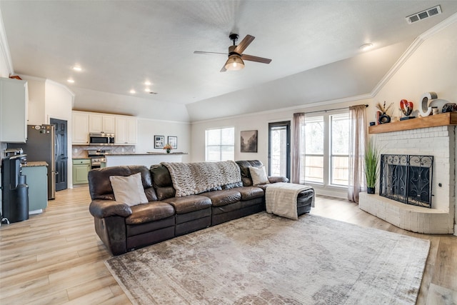 living room with lofted ceiling, crown molding, light wood-type flooring, ceiling fan, and a fireplace