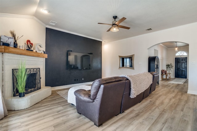 living room with crown molding, ceiling fan, a fireplace, and light wood-type flooring