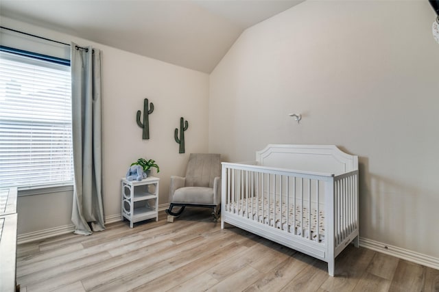 bedroom with a crib, vaulted ceiling, and light hardwood / wood-style floors