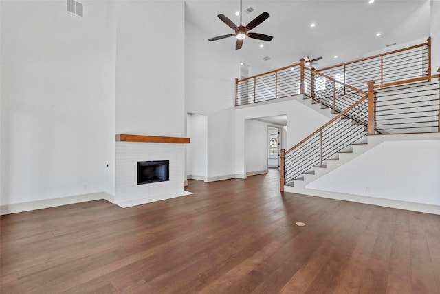 unfurnished living room with visible vents, a ceiling fan, wood finished floors, stairs, and a brick fireplace