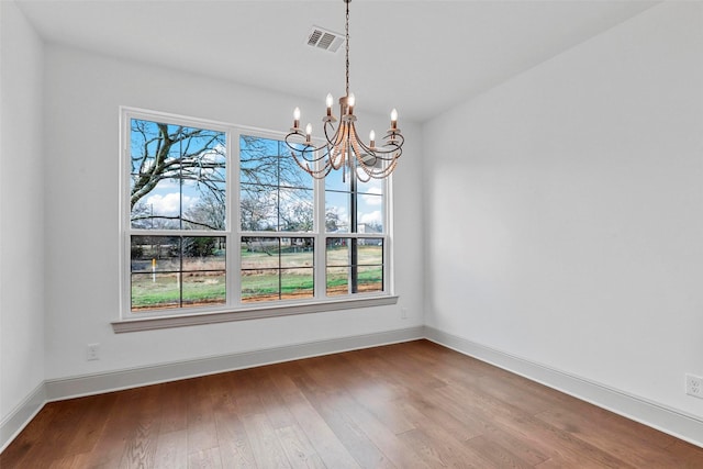 unfurnished dining area with an inviting chandelier, visible vents, baseboards, and wood finished floors