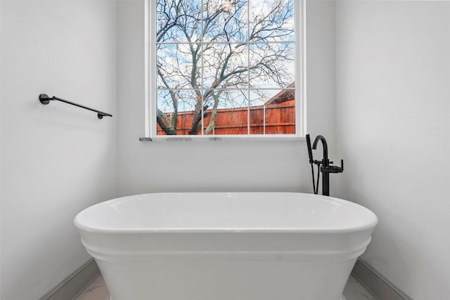 full bathroom featuring a freestanding tub, baseboards, and marble finish floor