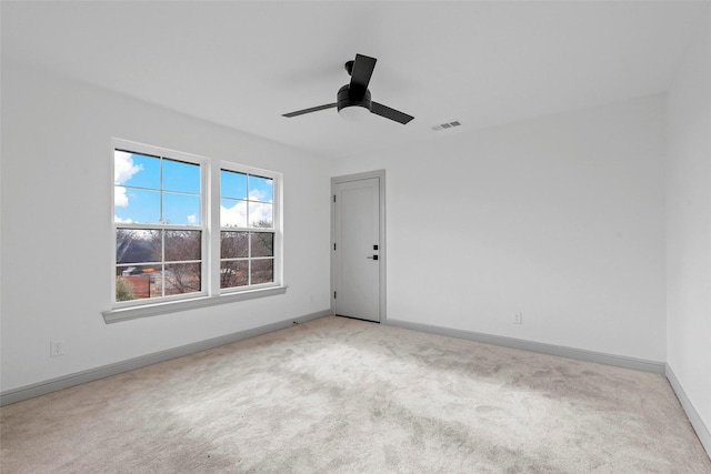 spare room with light colored carpet, ceiling fan, visible vents, and baseboards