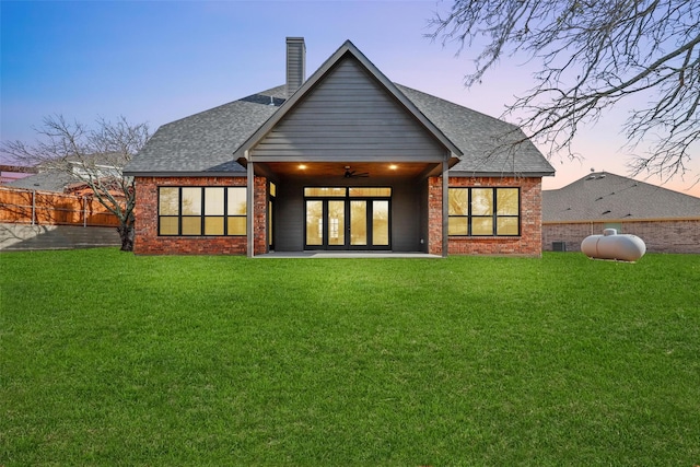 back of house at dusk featuring brick siding, a lawn, fence, and a ceiling fan