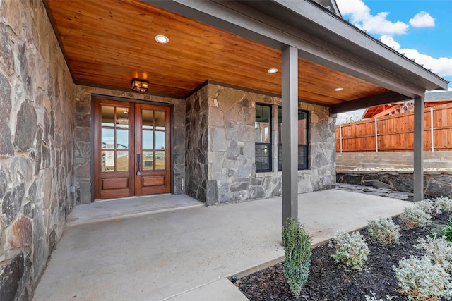 view of exterior entry featuring stone siding, french doors, fence, and a patio