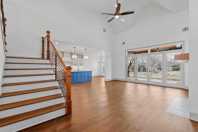 unfurnished living room with visible vents, stairway, a sink, wood finished floors, and ceiling fan with notable chandelier