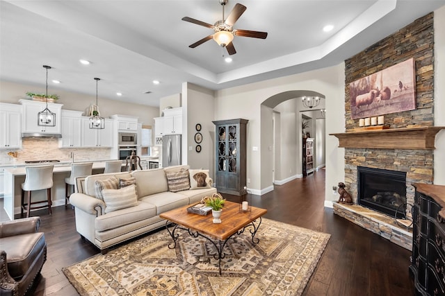 living room with ceiling fan, a fireplace, a tray ceiling, and dark hardwood / wood-style floors