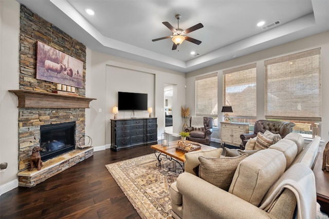 living room featuring a raised ceiling, a stone fireplace, dark hardwood / wood-style floors, and ceiling fan