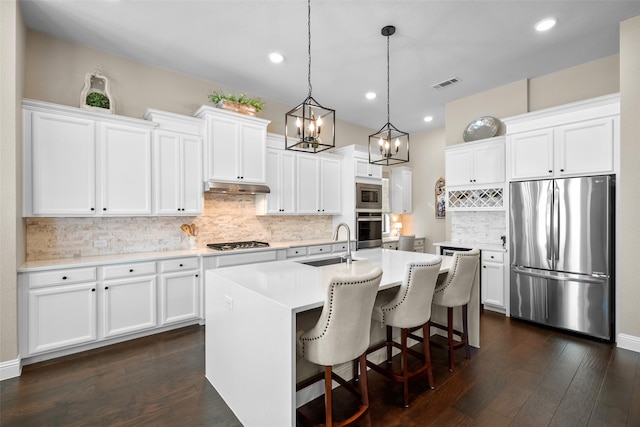 kitchen with white cabinetry, sink, hanging light fixtures, stainless steel appliances, and a center island with sink