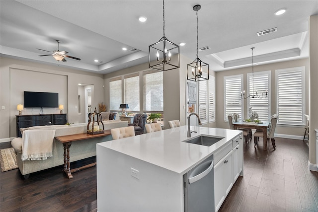 kitchen with sink, a tray ceiling, decorative light fixtures, and a kitchen island with sink