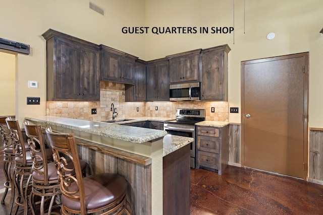 kitchen featuring appliances with stainless steel finishes, sink, a kitchen bar, light stone counters, and kitchen peninsula