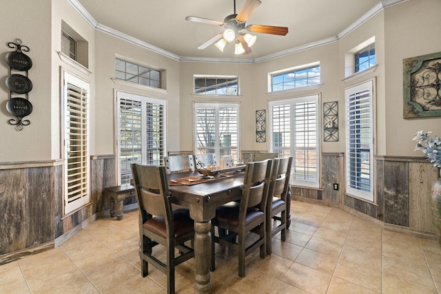 tiled dining room with crown molding, wooden walls, ceiling fan, and a high ceiling