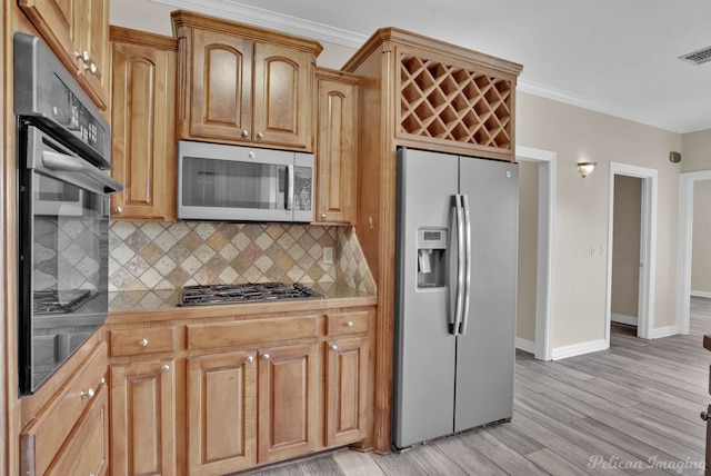 kitchen featuring stainless steel appliances, tile counters, ornamental molding, decorative backsplash, and light wood-type flooring