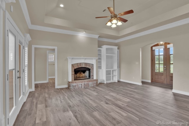 unfurnished living room with french doors, a brick fireplace, ornamental molding, a raised ceiling, and light hardwood / wood-style floors