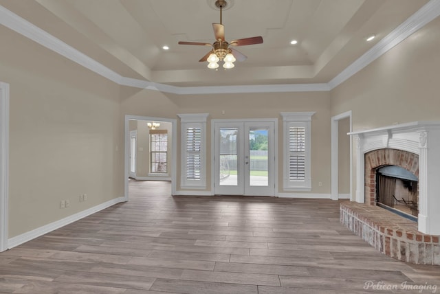 unfurnished living room with a brick fireplace, light hardwood / wood-style floors, french doors, and a raised ceiling