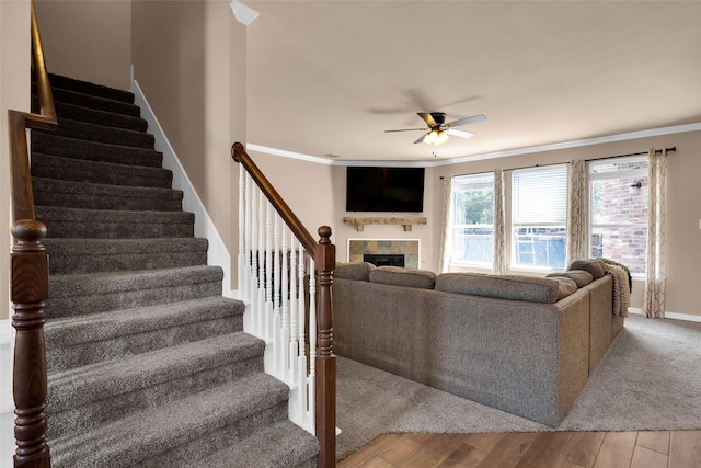 living room with crown molding, a fireplace, ceiling fan, and light wood-type flooring