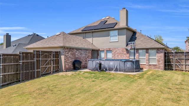 rear view of property featuring a yard, a covered pool, and solar panels