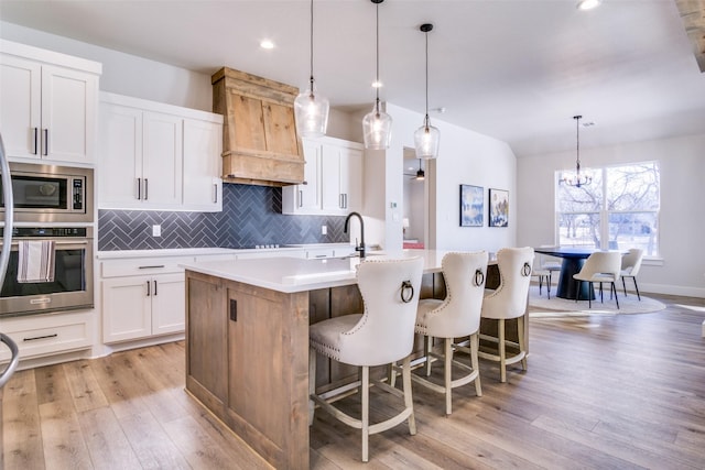 kitchen featuring a kitchen island with sink, hanging light fixtures, white cabinets, and appliances with stainless steel finishes