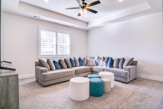 carpeted living room with a tray ceiling and ceiling fan