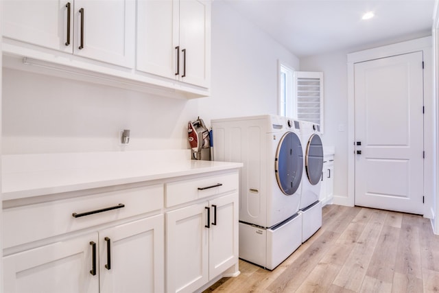 clothes washing area featuring cabinets, washer and clothes dryer, and light hardwood / wood-style floors