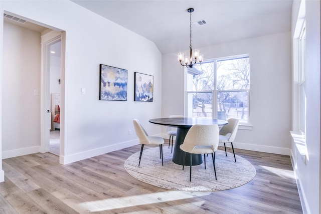 dining space with a notable chandelier, vaulted ceiling, and light wood-type flooring