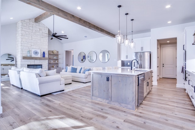 kitchen with pendant lighting, ceiling fan, stainless steel appliances, white cabinets, and a large island with sink