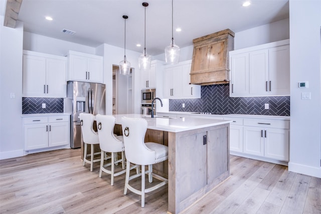 kitchen featuring sink, stainless steel appliances, white cabinets, a center island with sink, and decorative light fixtures