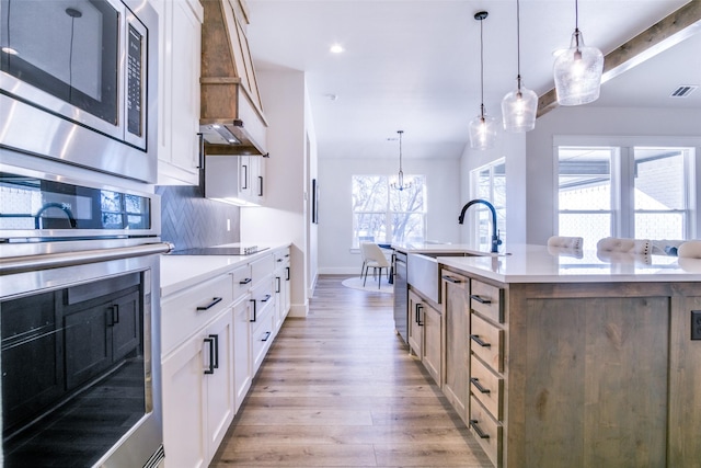 kitchen with tasteful backsplash, a kitchen island with sink, stainless steel appliances, light hardwood / wood-style floors, and white cabinets