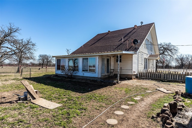 rear view of house featuring a yard, roof with shingles, and fence