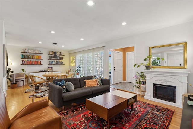 living room with recessed lighting, a glass covered fireplace, and light wood-style flooring