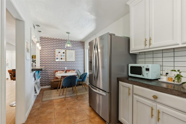 kitchen with white microwave, wallpapered walls, an accent wall, dark countertops, and stainless steel fridge