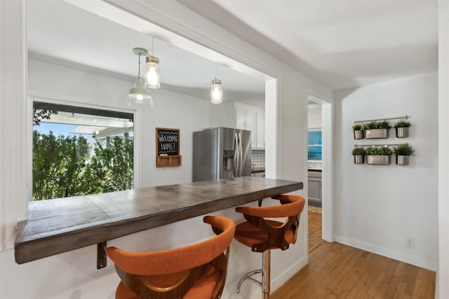 kitchen with baseboards, decorative light fixtures, light wood-style floors, stainless steel refrigerator with ice dispenser, and white cabinets