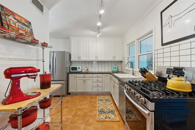 kitchen with sink, light tile patterned floors, appliances with stainless steel finishes, white cabinets, and backsplash