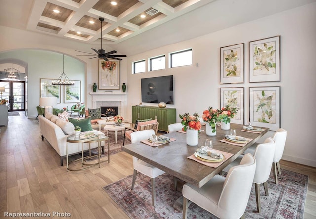 dining room featuring coffered ceiling, light wood-type flooring, beamed ceiling, a towering ceiling, and a high end fireplace