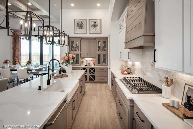 kitchen featuring appliances with stainless steel finishes, pendant lighting, sink, light stone counters, and custom range hood