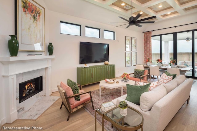 living room with coffered ceiling, ceiling fan, a fireplace, and beamed ceiling