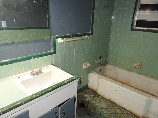 bathroom featuring vanity, tiled shower / bath combo, and tile walls