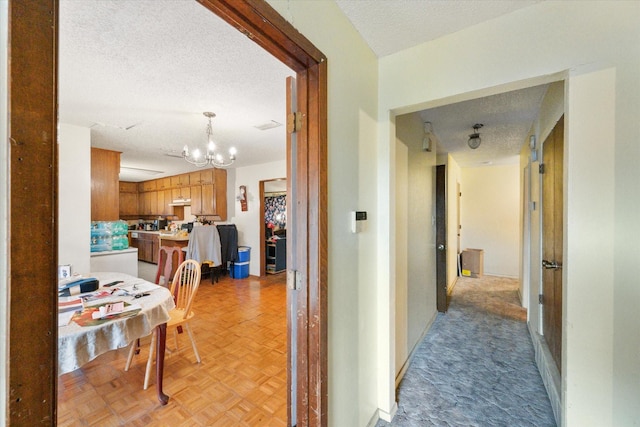 hall with a chandelier, a textured ceiling, and light parquet floors