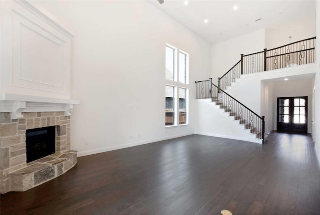 unfurnished living room featuring a stone fireplace, dark wood-type flooring, french doors, and a towering ceiling