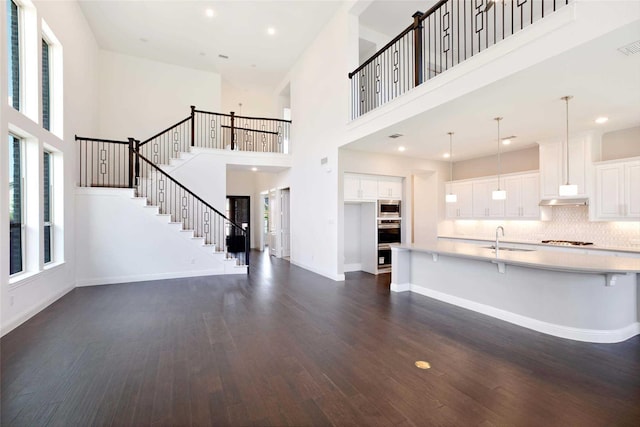 unfurnished living room with a high ceiling, sink, and dark hardwood / wood-style flooring