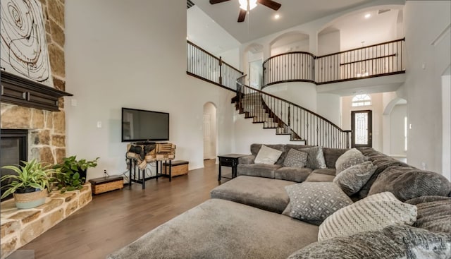 living room featuring a stone fireplace, dark wood-type flooring, and ceiling fan