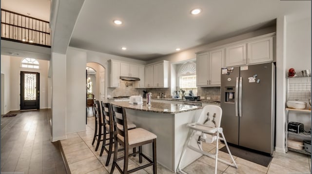 kitchen with white cabinetry, stainless steel fridge with ice dispenser, a healthy amount of sunlight, and stone counters