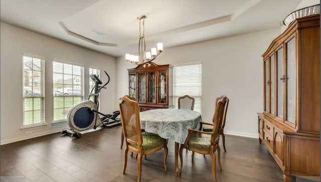 dining area with dark wood-type flooring, a notable chandelier, and a tray ceiling