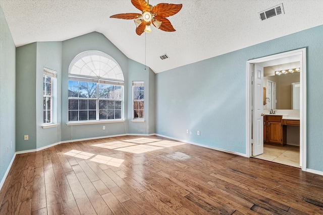 empty room with ceiling fan, vaulted ceiling, a textured ceiling, and light wood-type flooring